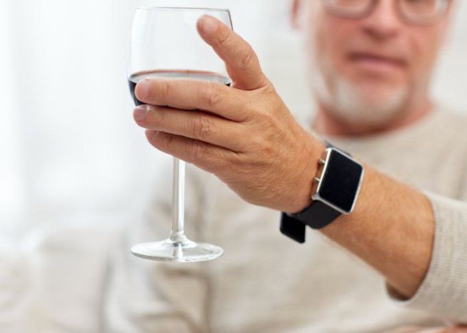 Senior w smartwatchu dla seniora z kartą SIM na ręce pije wino