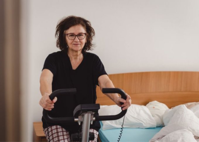 Seniorka dba o zdrowie trenując na rowerze stacjonarnym dla seniora